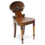 An early 19thC mahogany hall chair, with a carved shell shaped back, a solid seat, on turned