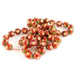 An enamel beaded necklace, the spherical beads in red enamel with green enamel leaf design, each set