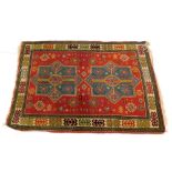 A Kazak` type rug, with two turquoise and red geometric medallions, on a red ground with one wide