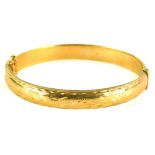 A 9ct gold hinged bangle, the top with scroll engraved design on a plain base, with safety chain,