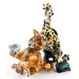 Two similar unusual pottery figures, depicting a giraffe drinking tea while seated and a cat begging