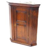 An early 19thC oak hanging corner cabinet, with a moulded cornice above a double panelled door,