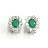 A pair of emerald and diamond cluster earrings, each set with oval emerald and surrounded by round