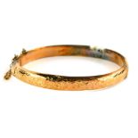 A 9ct gold hinged bangle, the hammered decoration upper tier on single clasp with safety chain,