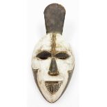 A heavily carved African tribal face mask, with pierced eyes and elaborate mouth, decorated in black