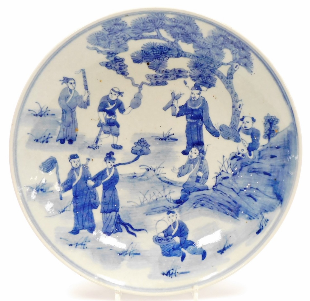 A Chinese blue and white plate, profusely decorated with figures before trees, with a double line