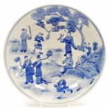 A Chinese blue and white plate, profusely decorated with figures before trees, with a double line