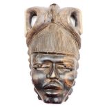 A heavily carved African tribal face mask, with elaborate hairstyle and pierced eyes, with shaped