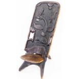 Tribal Art. A carved African hardwood seat, the tall back with carvings of fish, on spoon inset