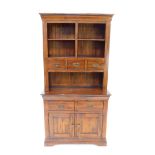 A mango wood cupboard bookcase, the outswept pediment over four division shelves above three