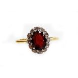 A garnet and diamond set dress ring, the central oval garnet dark red in colour surrounded by tiny d