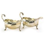 A pair of Elizabeth II silver sauce boats, each with a shaped border, a scroll cast handle and three