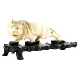 A 19thC oriental carved ivory figure of a prowling lion, (AF), 16cm long, on contemporary hardwood