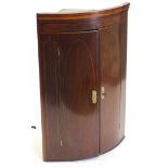 A 19thC mahogany and boxwood strung bow fronted corner cabinet, with two doors enclosing shelves,