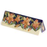 A Moorcroft pottery triangular plaque, decorated to one side with flowers, possibly wisteria, on a