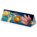 A Moorcroft pottery triangular plaque, decorated to one side with a dragonfly, fruits, flowers,