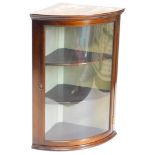 A bowfronted mahogany hanging corner cabinet, with a moulded cornice above a single glazed door