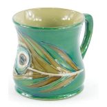 A Moorcroft pottery mug, decorated with a peacock feather, on a green ground, 8.5cm high.