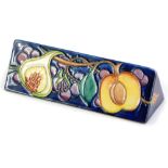 A Moorcroft pottery triangular plaque, decorated to one side with fruit, to include a peach, a fig