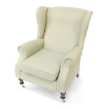 A Parker Knoll wing back armchair, upholstered in patterned green fabric, raised on turned legs, bra