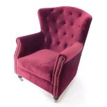 A wing back armchair, upholstered in purple button back velvet, raised on ebonised turned legs, on c