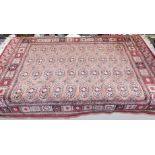 A Bokhara machine made wool rug, red ground with four rows of ten Teke style guls, 182cm x 118cm.