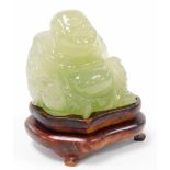 A 20thC Chinese jade coloured glass figure of a Buddha, on a hardwood stand, 10cm high overall.