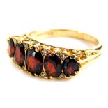 A 9ct gold garnet set gypsy ring, with five garnets and tiny diamond set shoulders, in a raised claw