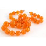 An orange hardstone graduated necklace, on a string strand, with gold plated clasp, the largest bead