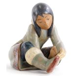 A Lladro porcelain model of a young Eskimo girl, inspecting her foot, in the seated position, printe