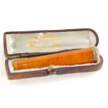 An early 20thC amber coloured cheroot holder, with yellow metal tip and scroll cartouche in fitted c