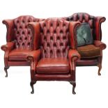 Three similar red studded leather Chesterfield type wing back chairs in 18thC style, each on cabriol