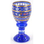A Bohemian style blue flash glass goblet, with gilt decoration and bands of flowers in coloured enam