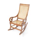 An early 20thC Bergere rocking chair, with cane work back and seat, heavily carved scroll arms and f