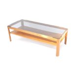 A vintage teak coffee table, the oblong smoky glass top raised on a plain stand, with plain rack ben