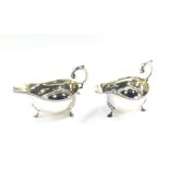 A pair of Edward VII silver sauce boats, with leaf scroll handles, gadrooned rims and raised on thre