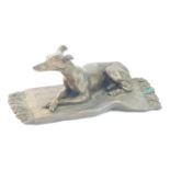 A bronzed plaster figure of a greyhound, modelled recumbent on a rug, stamped OFA, 9.5cm wide. (AF)