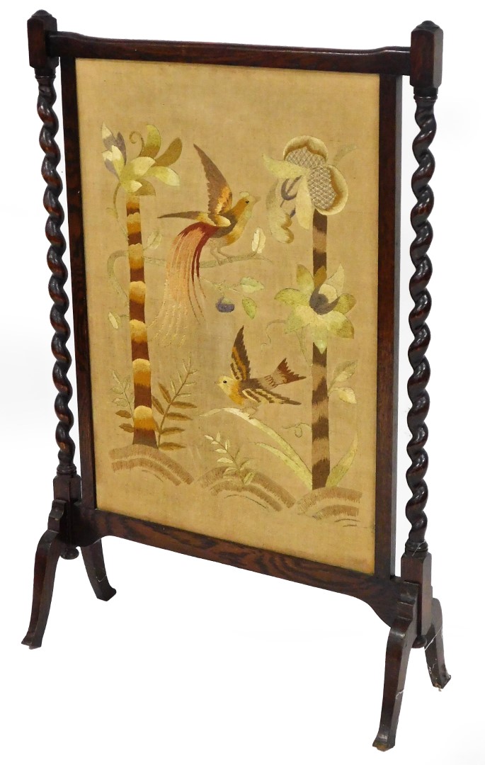 A late 19thC oak framed fire screen, the rectangular centre raised and embroidered with exotic birds