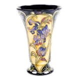A Moorcroft floral flared vase, depicting flowers on a dark blue and yellow ground with green Moorcr