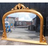 A modern gilt framed over mantel mirror, with arched top, and fleur de lis finial, with rose twist b