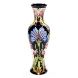 A Moorcroft stem vase, decorated with various flowers, on a dark blue and cream ground, with Moorcro