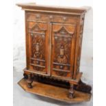An early 20thC carved oak wall cabinet, the two doors each with scroll and harp decoration, on a pin