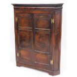 An early 19thC oak freestanding corner cupboard, with double panel doors, the plain interior set wit