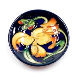 A Moorcroft pin dish, on a dark blue ground decorated with orange flowers, with green stamp to under