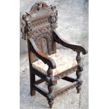A carved oak hall chair, the back with faces, berries, flowers and leaves, on a later upholstered se
