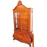 A cherry wood bombe display cabinet, the shell carved pleated top with an oval floral panel above tw