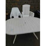 A white plastic garden table and seven various chairs.