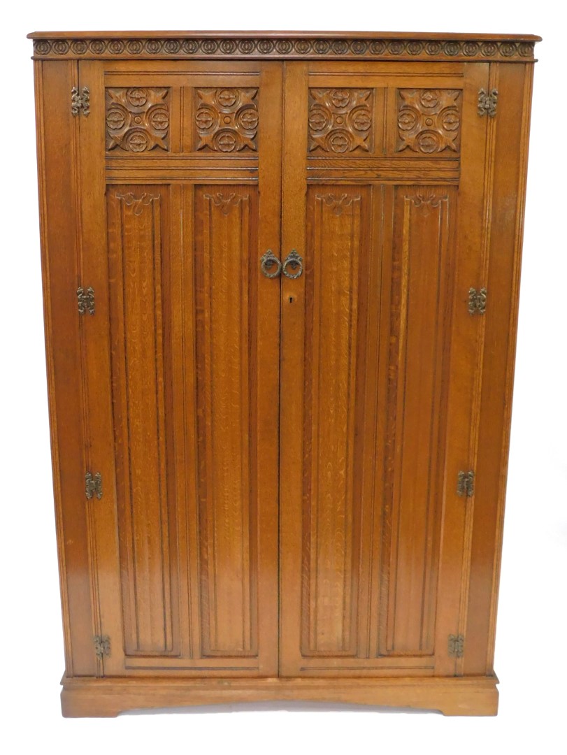 An Elizabethan style oak double wardrobe, with foliate and linen fold carved panelled doors, raised