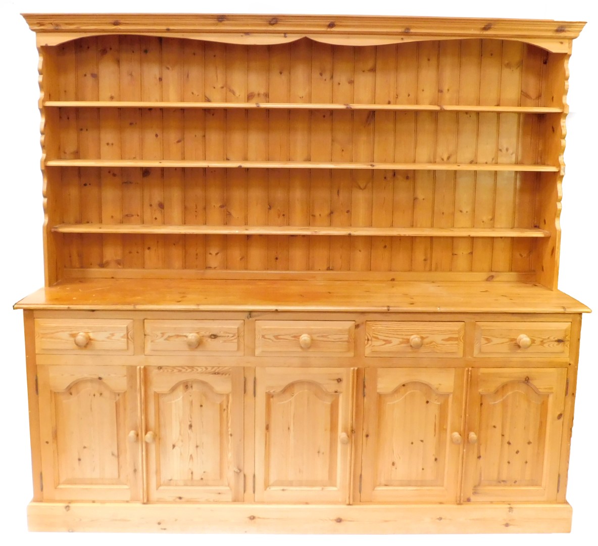 A pine dresser, the outswept pediment over a three shelf plate rack, above five short drawers, over