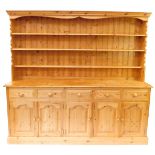 A pine dresser, the outswept pediment over a three shelf plate rack, above five short drawers, over
